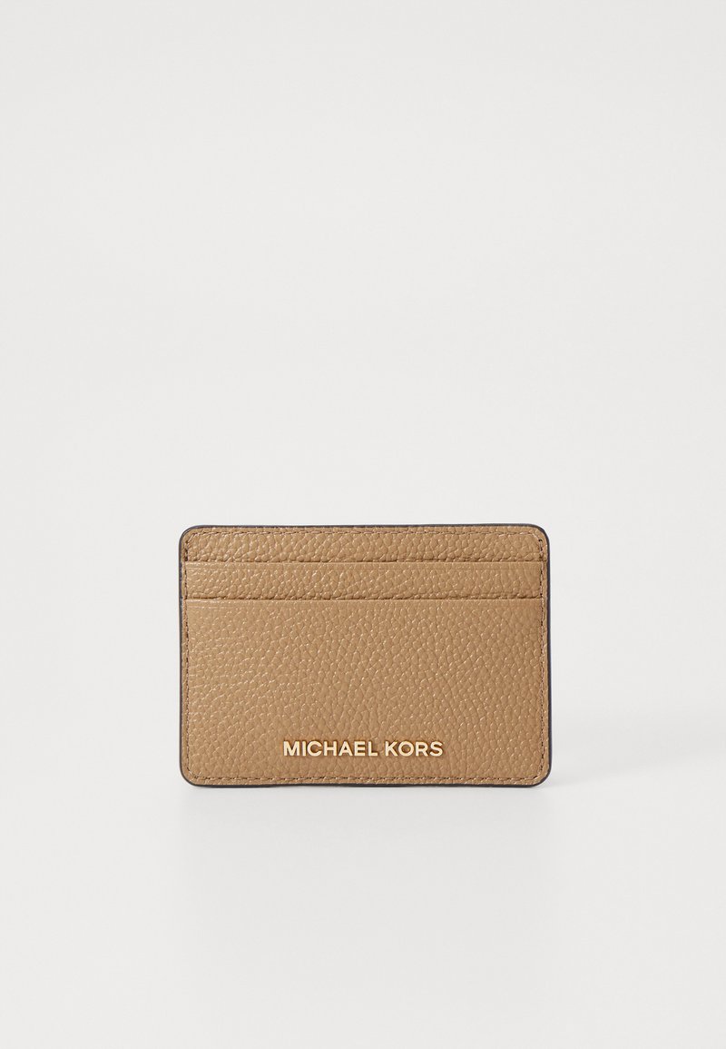 Tan spalvos odinis kortelių laikiklis su tekstūruota paviršiumi, turintis keturis kortelių lizdus ir iškilmingą "MICHAEL KORS" logotipą apačioje.