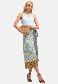 Light blue sleeveless top with decorative trim, paired with a patterned maxi skirt in blue, cream, and brown. Woven clutch and brown heels.
