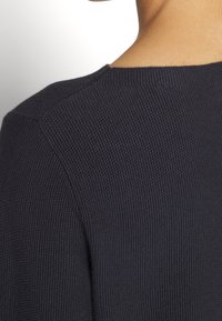 Gros plan sur le haut du dos et le cou d'une personne portant un pull en maille texturée bleu marine foncé avec un col rond.