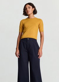 Haut jaune à manches courtes avec un col rond, associé à un pantalon large bleu marine à boutons sur le devant. Texture lisse, coupe ajustée.