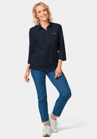 Marineblauwe polo met lange mouwen en knoopsluiting, gecombineerd met blauwe spijkerbroek en witte sneakers, met lichte stikdetails.