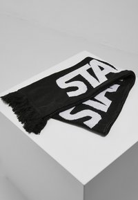 Asciugamano nero con testo bianco "STA", bordi frangiati, forma rettangolare, texture morbida e un design decorativo su un lato.