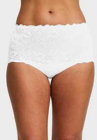 Vrouw in hooggesneden witte kanten ondergoed met een bloemenpatroon, weergegeven van de taille tot de bovenbenen op een effen achtergrond.