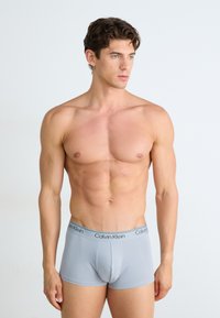 Bañador gris de Calvin Klein con una textura suave y una cinturilla con logo. El ajuste es ceñido y la tela parece suave y elástica.
