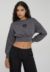 Szara, krótka bluza z długimi rękawami, z czarnym graficznym motywem w kształcie ust oraz napisem „Więcej miłości, por favor” z przodu. Miękka faktura materiału.