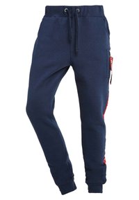 Navyblaue Jogginghose mit einem Kordelzugbund, schmal zulaufenden Beinen, einer seitlichen Reißverschlusstasche und einem roten gemusterten Akzent an der Seite. Weicher Stoff.