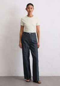 Jasno beżowa koszulka z okrągłym dekoltem połączona z szerokimi spodniami dżinsowymi w ciemnym kolorze, posiadającymi przednie kieszenie i kontrastowe szwy.