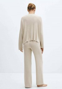 Ensemble de vêtements d'intérieur en maille beige comprenant un pull ample et court avec des manches larges et un pantalon droit assorti, fabriqué en matériau doux et texturé.