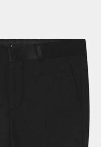 Černé kalhoty s hladkým materiálem, mají plochý přední díl, boční kapsy a elegantní pas. Minimalistický design bez viditelných vzorů.