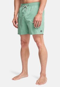 Pantaloni da bagno verdi con vita elastica e cordoncino regolabile, dotati di una tasca laterale e un piccolo logo.