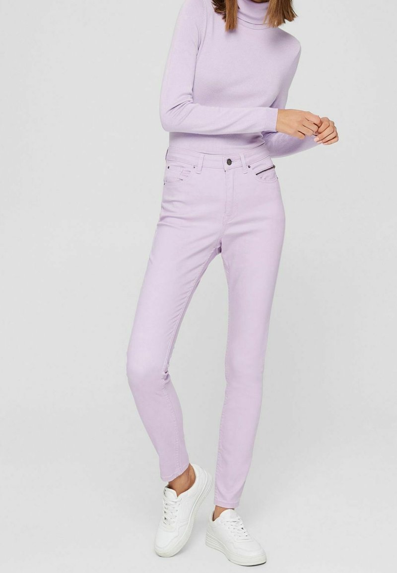 Fialové vysoké džíny s úzkým střihem, čtyřmi kapsami a zipovým zapínáním. Doplněné světle fialovým rolákem a bílými teniskami.