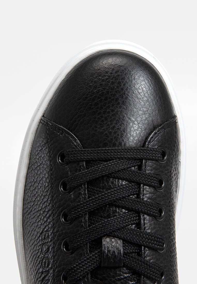 Czarne skórzane sneakersy o teksturowanej powierzchni, z czarnymi sznurowadłami, metalowymi oczkami i białą gumową podeszwą. Zbliżenie na obszar palców.