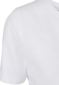 Detailní záběr na bílé tričko s výstřihem do V a krátkým rukávem, který ukazuje текстuru látky a švy na rameni a rukávu.