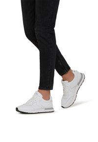 Weiße SportSneaker aus glattem Leder mit Maschelementen, schwarzer Gummisohle und Schnürverschluss, kombiniert mit schwarzen Jeans.