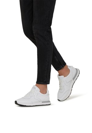 Scarpe da ginnastica bianche in pelle liscia con dettagli in rete, suola in gomma nera e chiusura con lacci, abbinate a jeans neri.
