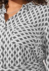 Camicia button-up in bianco e nero, con un motivo a diamante, taschino sul petto e un tessuto liscio con una leggera lucentezza.