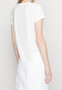 Vit kortärmad t-shirt med rund halsringning och rak skärning, tillverkad av mjukt bomullstyg. Har en slät textur.