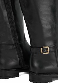 Black leather mid-calf boots with side zipper and gold buckle detail on strap above the heel, featuring lugged rubber soles.