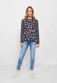 Blusa a maniche lunghe di colore blu navy con motivo floreale in rosa, bianco e verde. Indossata con jeans azzurri chiari e sneakers bianche alte.