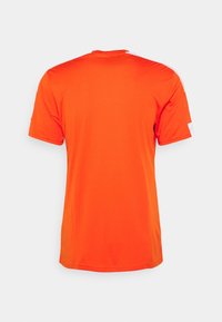 Kraťasový sportovní shirt v jasně oranžové barvě, s kulatým výstřihem a bílými akcenty na ramenou, vyrobený z lehké, hladké tkaniny.