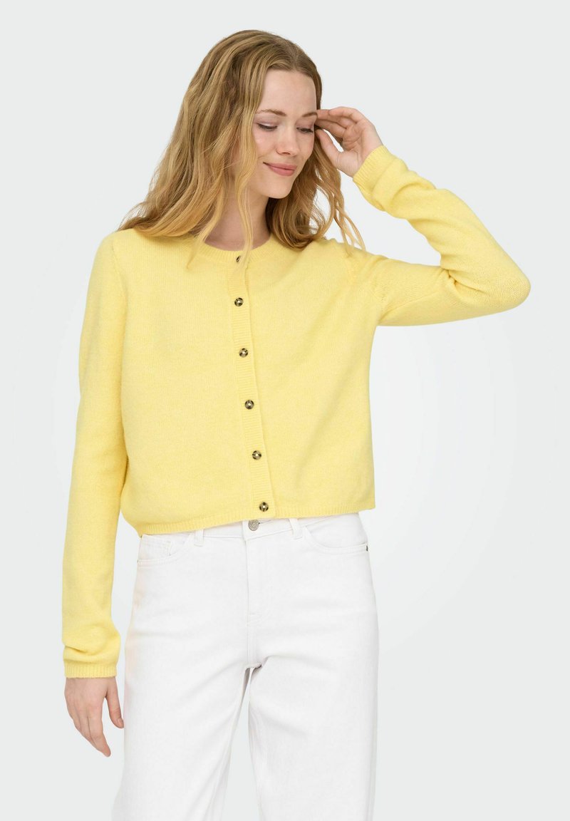 Gul strikket cardigan med rund hals, knappelukking foran og lange ermer. Teksturert stoff vist mot en lys bakgrunn.