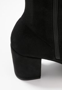 Sort ruskinds-ankelstøvle med en afrundet blokhæl, der har en sidelås og en glat tekstur. Sømme detaljer er synlige på overdelen.