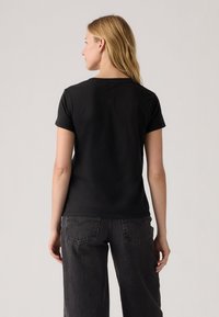 Schwarzes kurzärmliges T-Shirt aus Baumwolle mit Rundhalsausschnitt. Einfaches Design, keine Muster oder sichtbaren Logos. Lässige Passform, getragen mit grauen Jeans.