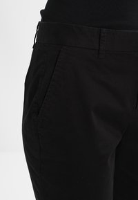 Pantalon noir en mélange de coton lisse, avec deux poches latérales, une coupe droite, et un design minimaliste sans motifs ni ornements visibles.