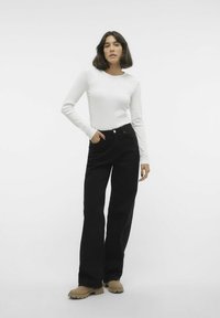 Witte blouse met lange mouwen, gecombineerd met hoge taille zwarte wijde broek en beige chunky schoenen, die een gladde stof en een op maat gemaakte fit toont.