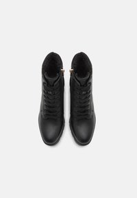 Bottines en cuir noir avec doublure en fausse fourrure, devant à lacets et zips sur les côtés ; texture lisse, bout arrondi et accents matériels minimalistes.
