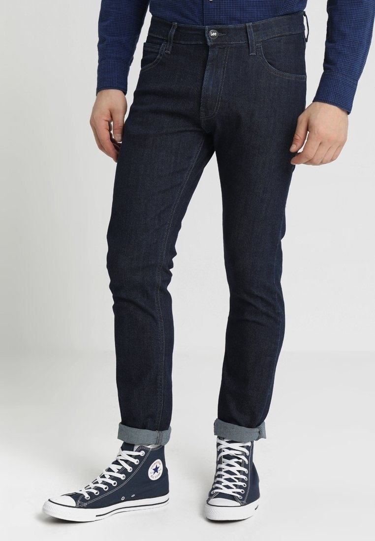 Mörkblå denimjeans med smal passform, med en klassisk femficksdesign, bältesloopar och knappstängning. Nedvikta ärmar och sneakers.