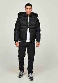 Črno puhovko z ruto s kapuco in umetnim krznenim robom, z zadrgo, prešito teksturo, nošeno čez belo grafično majico in združeno s črnimi cargo hlačami.