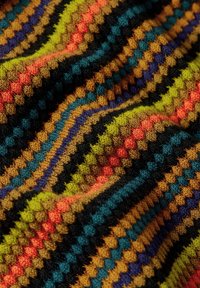 Gebreide stof met een meerkleurig zigzagpatroon in groene, oranje, blauwe en zwarte tinten. Zachte textuur met zichtbare stiksels.