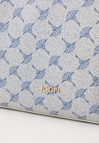 Borsa in tessuto stampato blu e bianco con un design floreale e un logo dorato "JOOP!" in basso. Superficie strutturata, forma compatta.