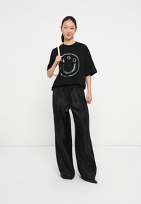 Camiseta negra oversized con un gráfico de una sonrisa plateada, combinada con pantalones negros holgados. El modelo sostiene un pequeño bolso rosa.