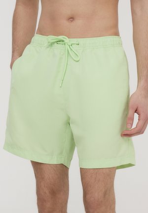 Costumi da bagno verde chiaro con vita elasticizzata e cordino, dotati di tasche laterali e un tessuto morbido e leggero.