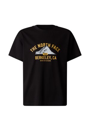 Person iført en sort The North Face t-shirt og mørkegrønne joggingbukser, der holder en matchende grøn taske og bærer sorte støvler.