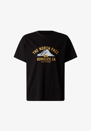 Person iført en sort The North Face t-shirt og mørkegrønne joggingbukser, der holder en matchende grøn taske og bærer sorte støvler.