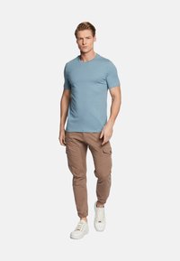 T-shirt azzurro chiaro con collo rotondo, slim fit. Abbinato a pantaloni cargo marroni con tasche laterali e sneaker bianche con punta rotonda.