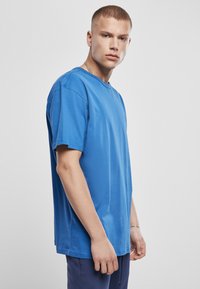 Tricou din bumbac albastru cu o croială lejeră, gât rotund, mâneci scurte și margine dreaptă. Textură netedă cu cusături și detalii minime.