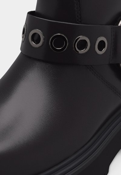 Μαύρο δερμάτινο μποτάκι αστραγάλου με φαρδιά φάσα που έχει πέντε μεγάλα ασημένια μεταλλικά κρίκους γύρω από τον αστράγαλο.