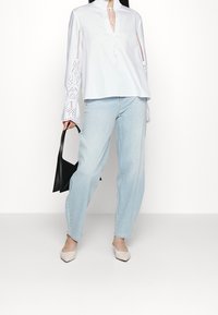 Vit blus med ögondetaljer på ärmarna, i kombination med ljusblå jeans och beige klackar. Svart handväska med en minimalistisk design.