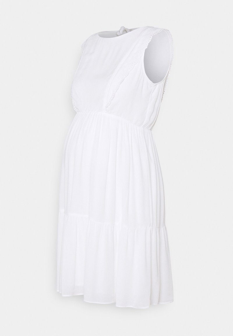Robe de maternité blanche avec un design sans manches, dentelle au niveau des épaules et un ourlet évasé froncé. Fabriquée à partir d'un matériau léger et doux.