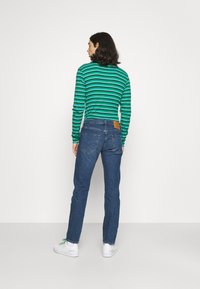 Camisa de mangas compridas às riscas verde e azul-marinho combinada com jeans azuis. Os jeans apresentam um retalho de couro castanho e bolsos traseiros clássicos. Sneakers brancos.