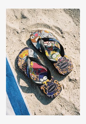 Paire de tongs colorées Havaianas avec des personnages de dessins animés sur une plage de sable à côté d'une serviette rayée bleue et blanche.