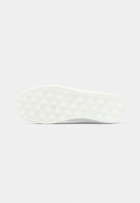 Semelle blanche de chaussure avec un motif de logo "CK" en relief répété sur un fond gris clair uni.