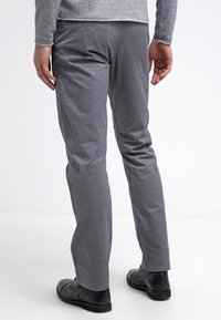 Graue Baumwollhose mit geradem Bein. Verfügt über eine glatte Textur und minimale Details. Getragen mit schwarzen Lederschuhen.