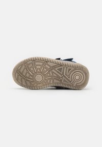 Suela de sneaker de goma con un patrón de agarre texturizado. Color marrón claro con surcos y círculos. Construcción resistente, diseñada para tracción.