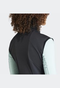 Black sleeveless vest featuring a textured back and side panels in mint green, with a high collar and smooth fabric finish.
