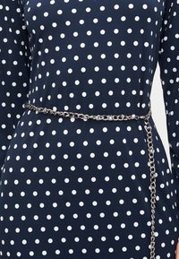 Μπλε φόρεμα navy με λευκά πουά, μακριά μανίκια και λεπτή ασημένια αλυσίδα ζώνη δεμένη γύρω από τη μέση.